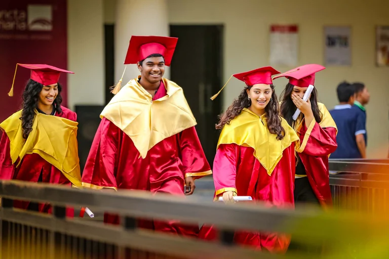 Smiling graduates in red and gold caps and gowns walking together after Sancta Maria International School graduation ceremony